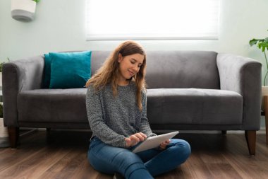 Güzel genç bir kadın oturma odasında yerde oturup tablet kullanıyor.
