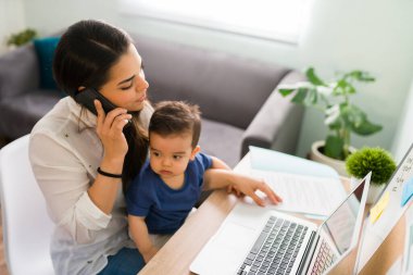 O evde bilgisayarla çalışırken ve telefonda konuşurken tatlı erkek bebek annesinin kucağında oturuyor.