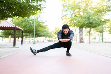 Atletik ve yakışıklı genç adam sabah koşusuna başlamadan önce koşuda bacaklarını esnetiyor.