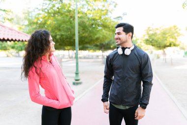 Sportif çift parkta egzersiz rutinleri arasında konuşuyor. Genç bir adam ve genç bir kadın etek giyiyor gülümsüyor ve flört ediyorlar. 