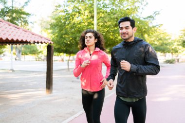 Çekici genç kadın ve genç adam spor kıyafetler giyip parkta birlikte koşuyorlar.