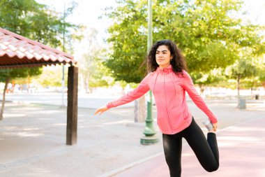 Spor kıyafetli genç bir kadın parkta antrenman yapmadan önce bacak kaslarını ısıtıyor.