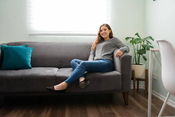 魅力的な若い女性の肖像画笑顔と彼女のアパートラウンジのソファでリラックス — ストック写真