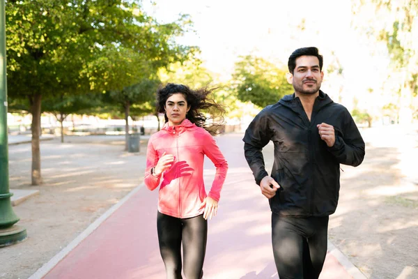 Front view of a fit and determined couple wearing sportswear running together in the park track