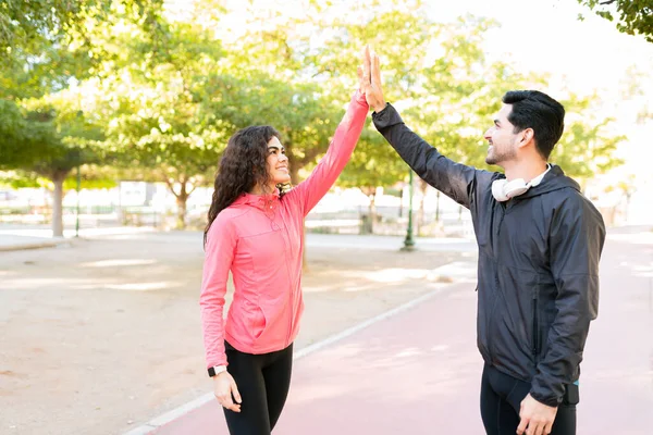 Attractive young woman and young guy in their 20s doing a high five for reaching their workout goals in the park