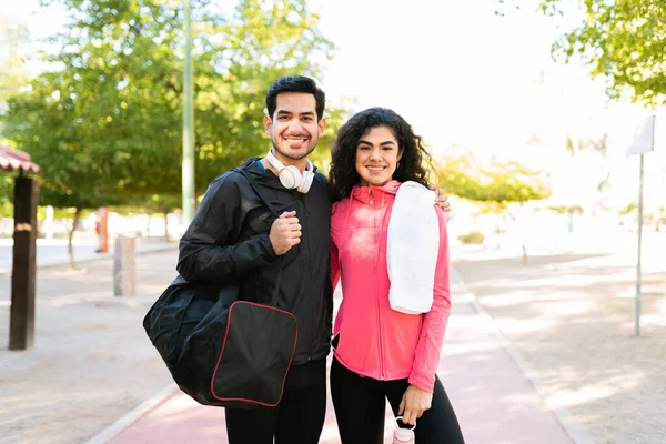 快乐而运动的年轻夫妇抱着一个体操袋 毛巾和水瓶在公园里玩耍 — 图库照片