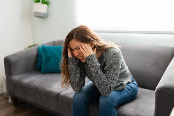 年轻女人坐在沙发上 脸上带着痛苦的表情 头痛或偏头痛的漂亮女人 — 图库照片