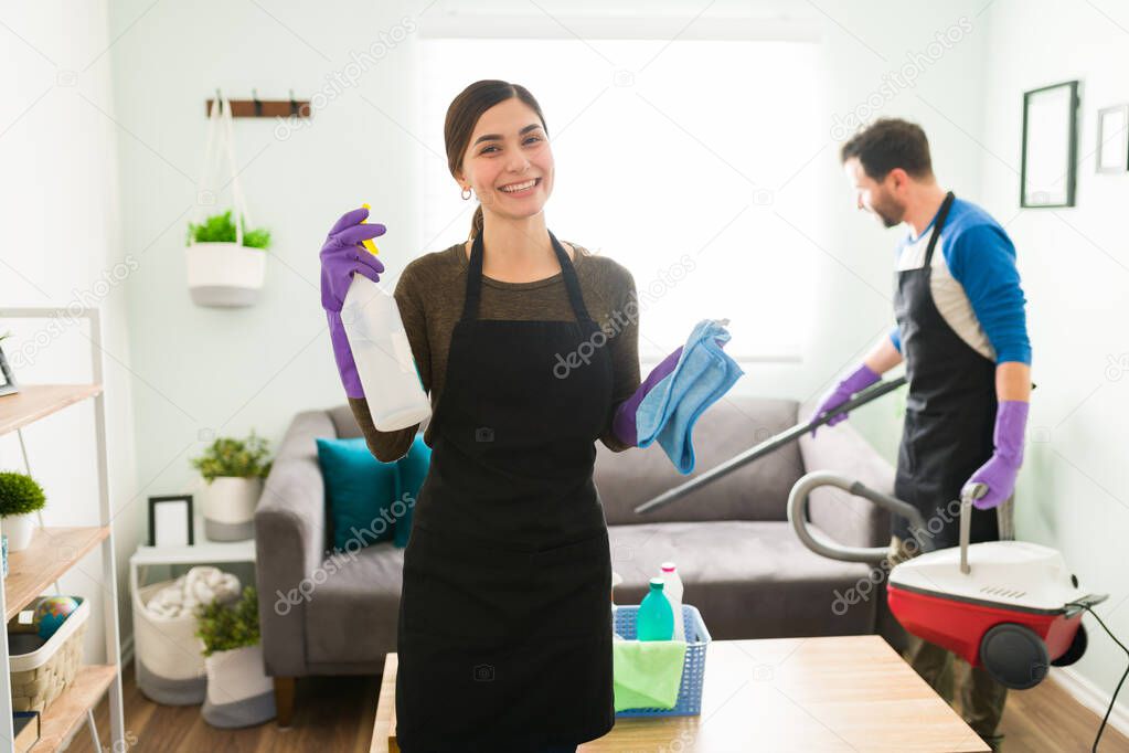 Beautiful young woman wearing an apron and gloves and enjoying cleaning her house together with her boyfriend