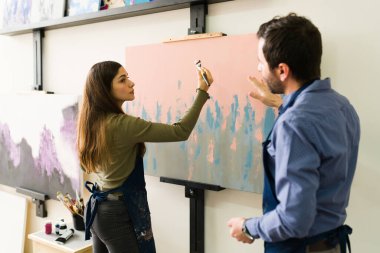 20 'li yaşlardaki genç bir kadın resim yapma tekniğini öğrenmek için sınıftaki bir erkek öğretmene ilgi gösteriyor. 