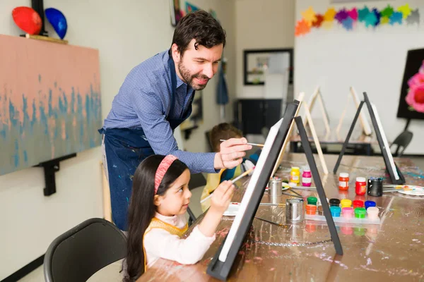Uśmiechnięty Nauczyciel Jest Szczęśliwy Pomaga Małej Dziewczynce Malować Płótnie Podczas — Zdjęcie stockowe