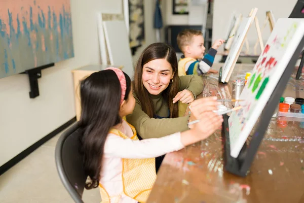 ヒスパニック系の女性のインストラクター笑顔と子供のための絵画クラス中にキャンバス上でペイントする方法の女の子を教える — ストック写真