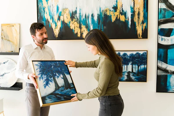 男画家把他的画展示给一个有兴趣从美术馆的附赠处购买一些艺术品的女客户 — 图库照片