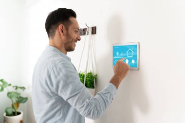 Hispanik bir adam akıllı ev sistemini kontrol etmek için tablet ekranını kullanırken gülümsüyor.
