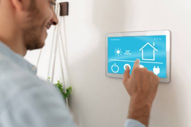 Akıllı ev aletlerini kontrol etmek için dokunmatik ekran kullanan genç bir adamın yakın çekimi.