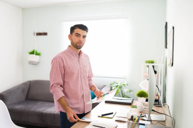 20 'li yaşlarda güzel bir gencin portresi. Elinde bazı evraklar var ve masasında ofis işi yapıyor. 