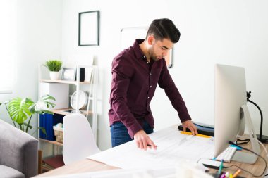 20 'li yaşlarda İspanyol bir adam evinde. Genç mimar çalışma masasında bir inşaat planı üzerinde çalışıyor. 