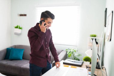Masasında oturan genç bir adamın iş arkadaşıyla konuşurken gülümsemesi ve konuşması. Çünkü evden çalışıyor.