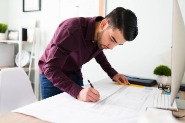 Yakışıklı ve kararlı bir genç adam yeni bir mimari proje için masasında bir plan tasarlıyor ve çiziyor.