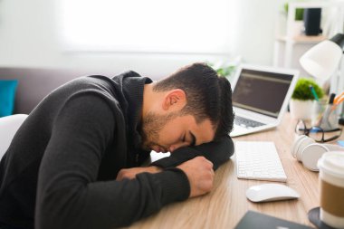 20 'li yaşlarda İspanyol bir adam ofis masasında dinleniyor. Yorgun ve stresli görünüyor çünkü yapacak çok işi var. 