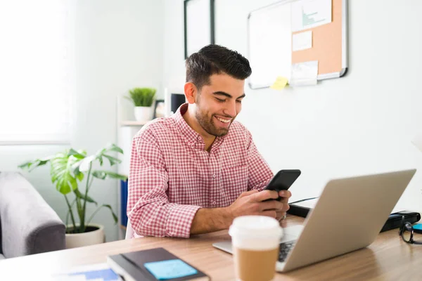 Jeune Homme Souriant Est Assis Son Bureau Regardant Son Smartphone — Photo