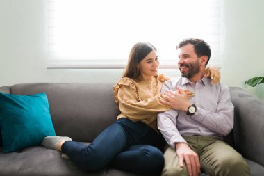 Romantik ve çekici bir çift oturma odasındaki kanepede oturuyor. Güzel kadın ve erkek sarılıyor ve gülümsüyor.