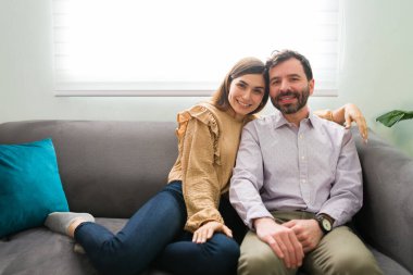 Latin yeni evliler kanepelerinde birbirlerine sarılıyorlar. Yakışıklı bir adam ve genç bir kadın, mutlu görünüyor ve oturma odasında oturuyor.