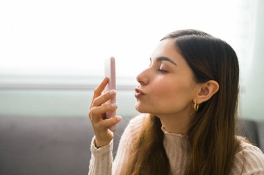 20 'li yaşlarda yakışıklı bir kadının akıllı telefonundaki bir randevu videosu sırasında sevgilisini öptüğünün profili.