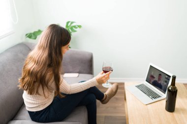 20 'li yaşlarda güzel bir kadının laptopuyla rahatlarken bir bardak şarap içerken ve sevgilisiyle romantik bir online randevu sırasında konuşurken yan görüntüsü. 