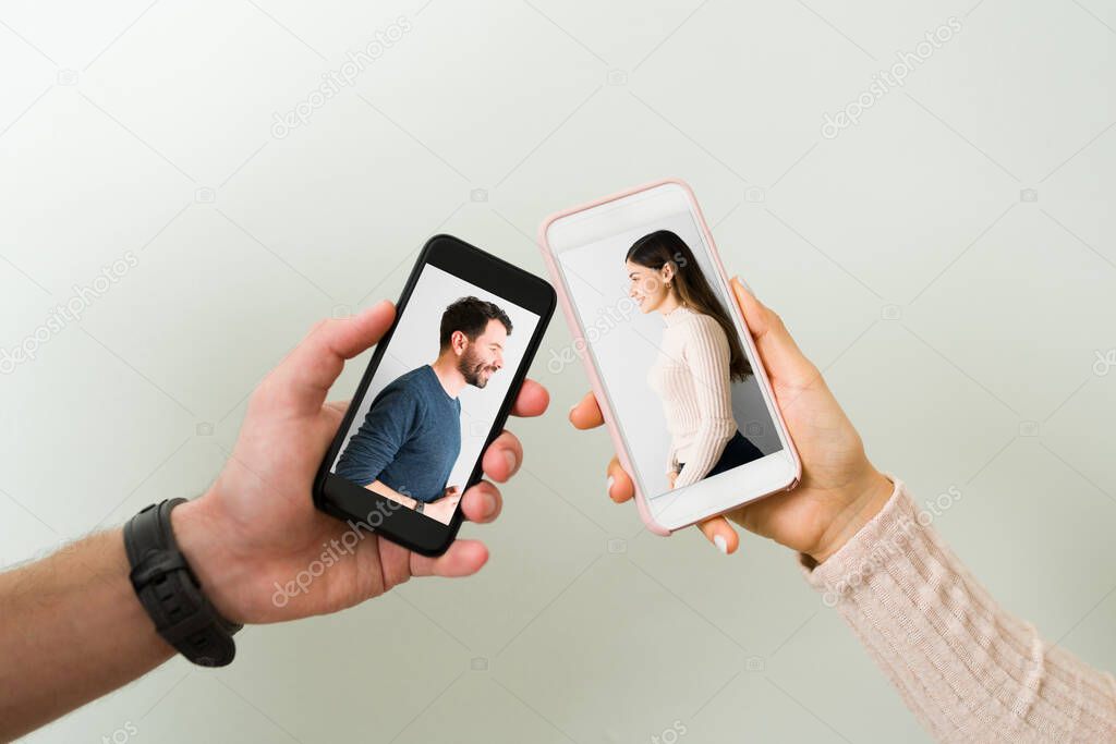 Close up of two hands holding smartphones with the photo of a smiling handsome man and pretty woman in a relationship. Love concept