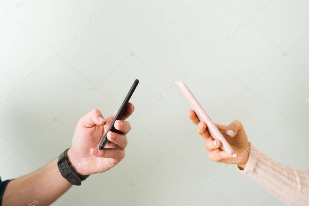 Hands of a young couple texting on their smartphones. Young woman and guy in a relationship are sending text messages 