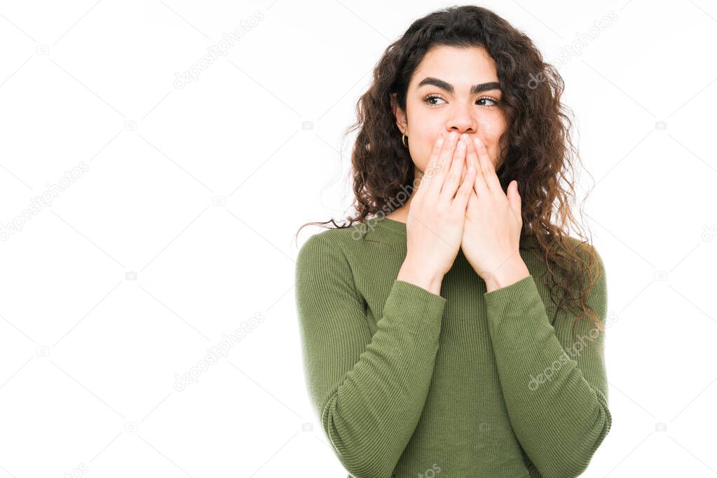 Beautiful hispanic woman looking shocked because she overheard a conversation. Young woman is covering her mouth to keep the secret 