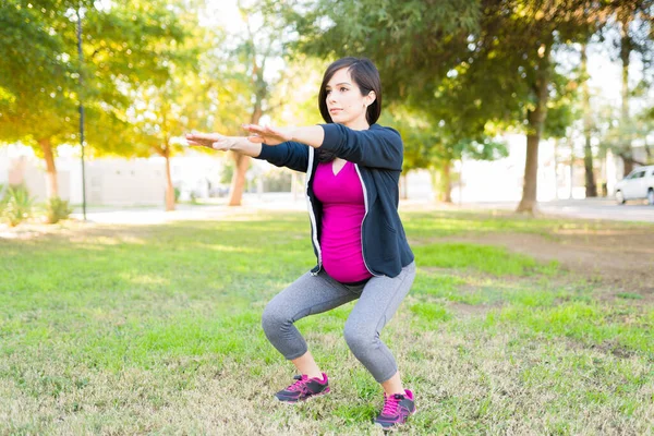 Pregnant woman with an active lifestyle doing squats exercises in the park to stay healthy and fit during her pregnancy