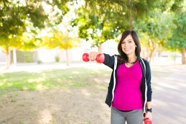 一个30多岁的漂亮女人和哑铃在公园里玩耍的肖像 快乐的孕妇户外运动 — 图库照片
