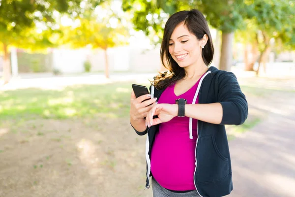 スマートウォッチとスマートフォンでワークアウトを追跡してくれる幸せな妊婦さん アクティブと健康的な女性チェック彼女の実行時間 — ストック写真