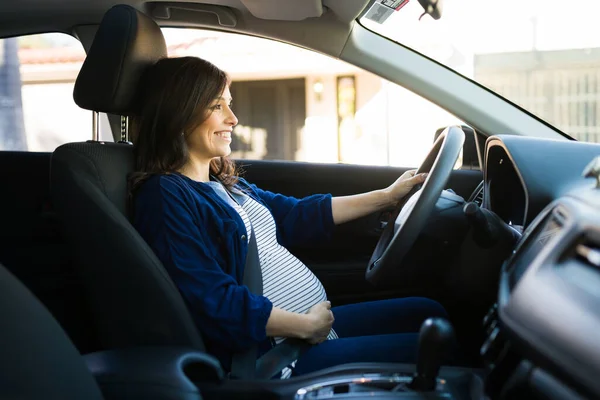 妊婦がシートベルトで車を運転して笑っている 美しいです女性で運転席で彼女のラウンド腹に触れる — ストック写真