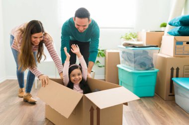 İspanyol aile oturma odasında mobilyalarını falan toplarken oyun oynuyorlar. Genç bir kadın ve bir adam küçük bir kızı karton bir kutunun içine itiyor.