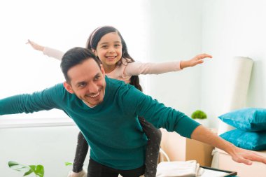 Küçük kızını sırtında taşıyan neşeli İspanyol bir baba. 30 'lu yaşlarındaki yakışıklı bir adam bir ilkokul kızını sırtında taşıyor ve onların evinde oynuyor.