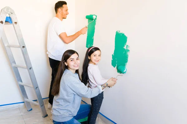 一个年轻的拉丁女人和一个小学小女孩的画像 她们一起拿着一个油漆滚筒 在客厅的墙壁上画画 — 图库照片
