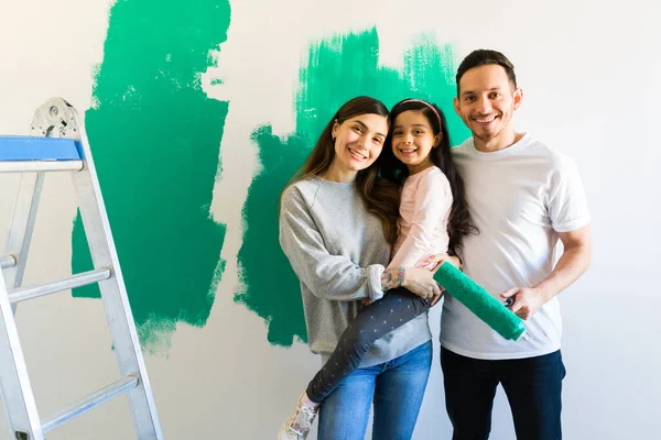 迷人的拉丁女子和男子与她的女儿愉快地摆姿势 同时粉刷和改造卧室 快乐的家庭重新装修他们的家 — 图库照片