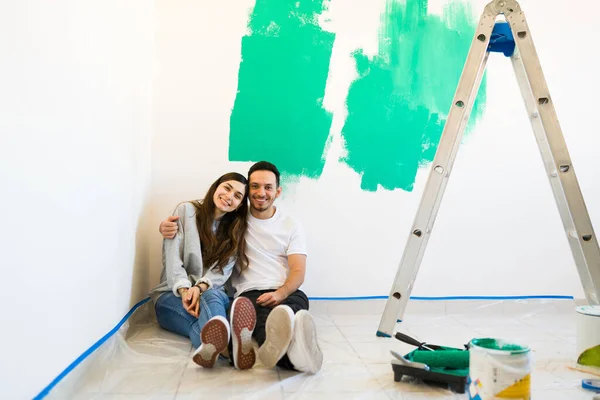 一个漂亮的年轻女子和一个英俊的男子搬进来后 正在粉刷墙壁 坐在新家的地板上拥抱爱人 — 图库照片