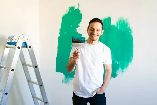 一个30多岁的英俊男人拿着粉刷滚筒微笑着 微笑的男人在他的新公寓或新家的墙上作画 — 图库照片