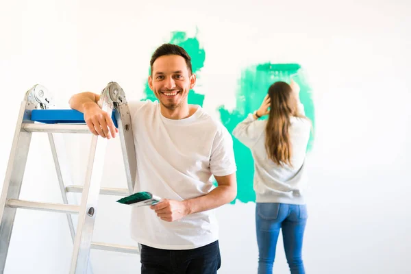 Handy husband painting the walls with a paint roller along her loving wife. Married couple redecorating and remodeling their new house