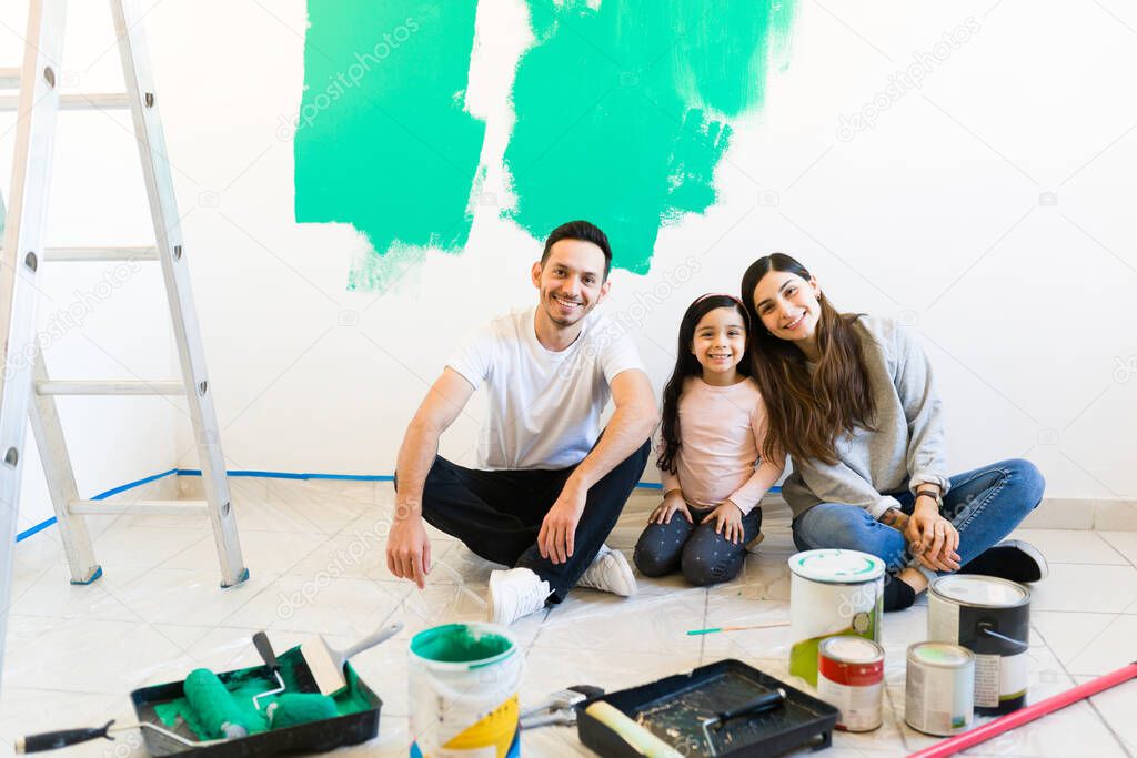 Young woman, man and girl doing a home renovation. Smiling and happy familiy looking at the camera while sitting on the floor