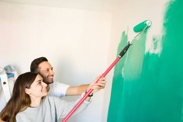 Happy married couple holding together a paint roller to paint green the white walls of their newly bought house