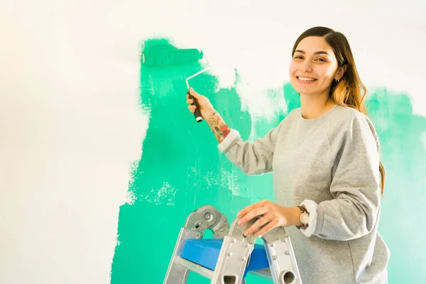 絵の具ローラーを持ちながら笑顔で20代の陽気な女性の肖像画 独立した女性は彼女の新しいアパートや家の壁を描く — ストック写真