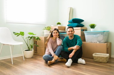 Karton kutular ve paketlerin önünde oturan evli bir çift var. Genç kadın ve erkek yeni evlerinin zemininde oturuyorlar.