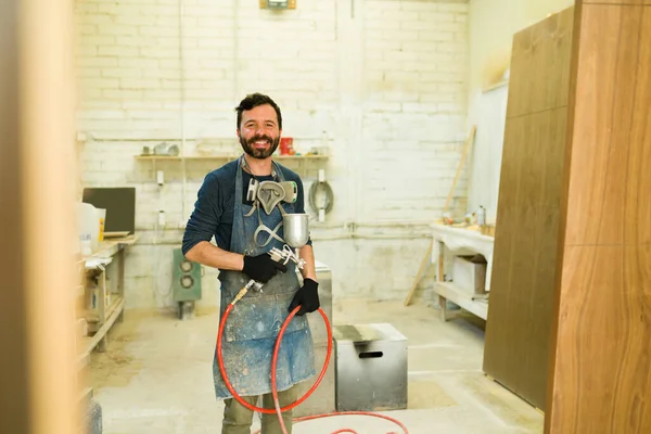 一个拿着呼吸器拿着喷枪的有魅力的男人的画像 在木材店的画室里 快乐的男性木匠 — 图库照片