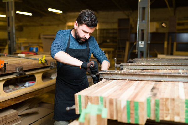 Трудолюбивый плотник мужского пола, работающий над сборкой кусков дерева. Красивый рабочий склеивает деревянные доски 