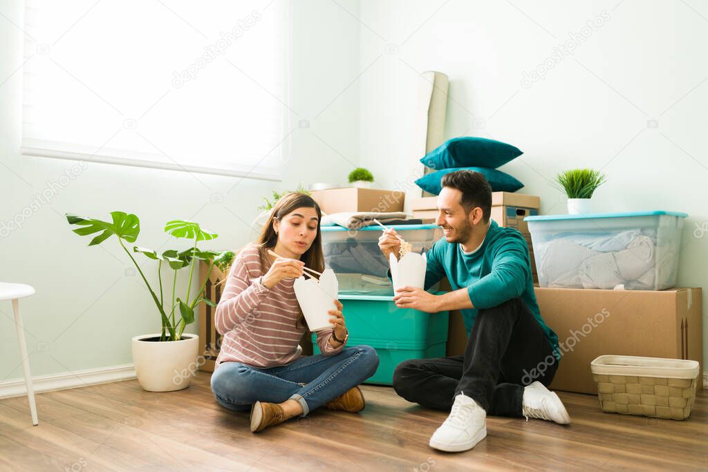 Beautiful wife and husband eating take out food on the floor of their new home or apartment. Latin couple taking a break to eat lunch after unpacking