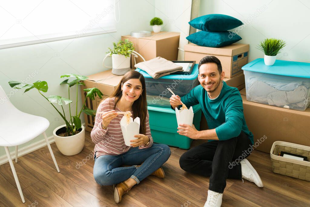 Couple in love eating fast food while sitting on the floor of their new home. Girlfriend and boyfriend eating lunch on their moving day